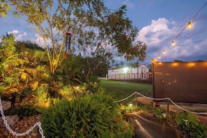 A landscaped garden with a pathway leading to a building with a white exterior and a deck. - Waterfall Suite ~Private Hot Tub~Zen at the Palms! (Homosassa)