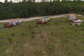 A residential area with multiple houses, a grassy field, and a dense forest in the background. - Waterfall Suite ~Private Hot Tub~Zen at the Palms! (Homosassa)