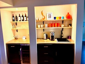 A compact kitchen with a sink, coffee maker, and wine bottles on shelves.