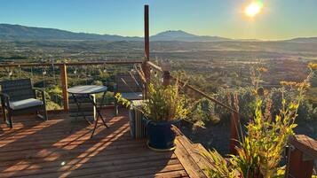 Eine Holzterrasse mit Gartenmöbeln, Kübelpflanzen und Blick auf ein Tal und Berge.