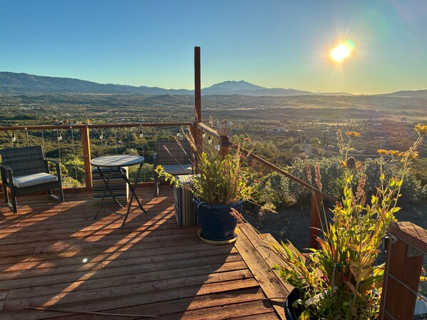 A wooden deck with outdoor furniture, potted plants, and a view of a valley and mountains.