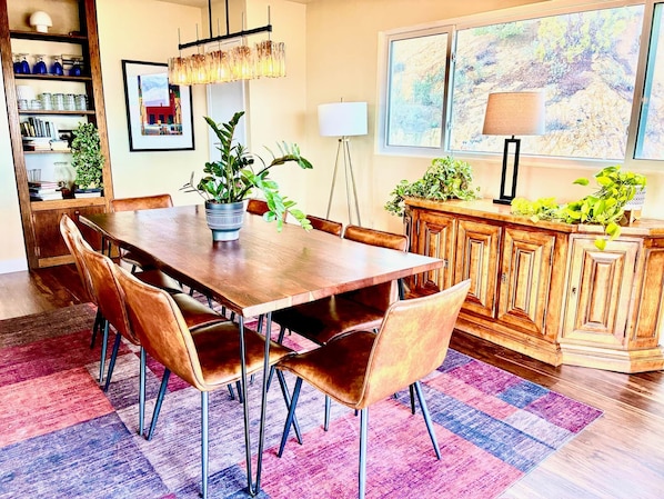 Un comedor con mesa de madera, sillas de cuero, una planta en maceta y alfombra colorida.