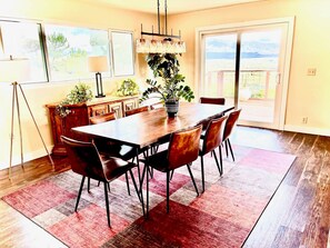 A dining area with a wooden table, six chairs, a red rug, and a potted plant.