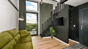 A modern living room with a green sofa, a wooden floor, a TV mounted on the wall, and a balcony with a view of the sky. - Luxurious home in Banfi with sauna (Banfi)