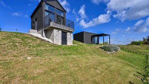 A modern two-story house with a balcony, situated on a grassy hill under a clear sky. - Luxurious home in Banfi with sauna (Banfi)