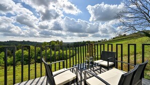 An outdoor seating area with a table and chairs, a bottle of wine, and a glass. The setting includes a metal fence and a view of a green landscape under a partly cloudy sky. - Luxurious home in Banfi with sauna (Banfi)