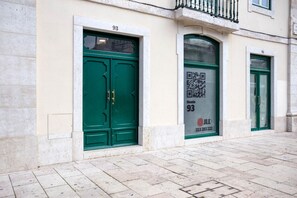 Two entrance doors with brass handles, set within a classical building with a balcony above.