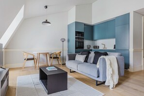 Relax in this stylish living space with a loft-style ceiling, grey sofa, and wooden floor.