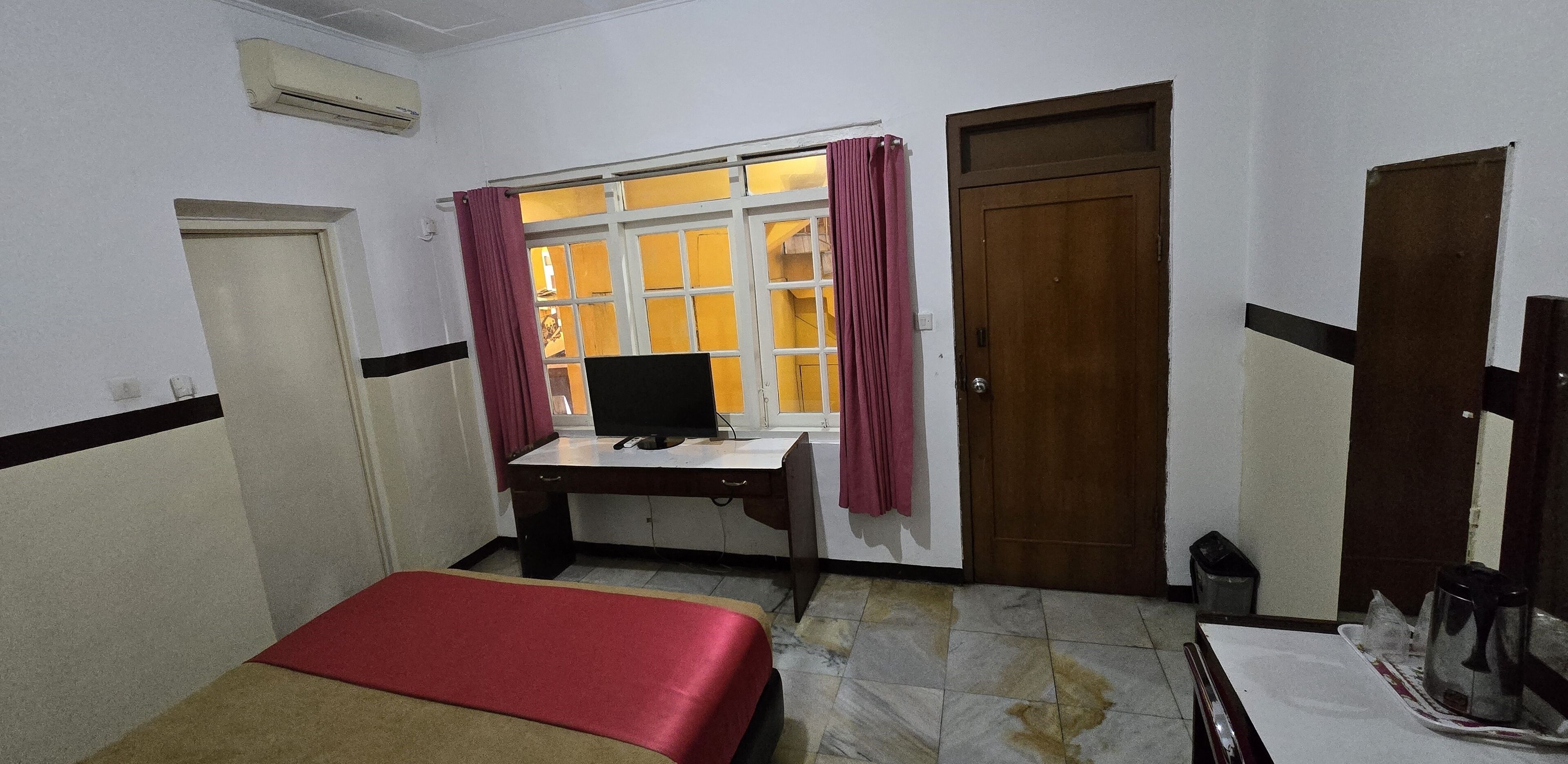 A small room with a bed, a desk with a computer, a window with curtains, and a door.