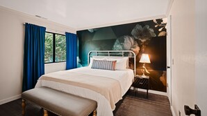 A bedroom with a bed, a bench, a nightstand with a lamp, and a mural on the wall.