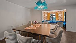 A dining area with a wooden table, grey upholstered chairs, and a decorative blue chandelier.