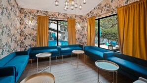 A room with blue sofas, a round table, and a large window with yellow curtains.
