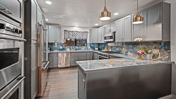 A modern kitchen with stainless steel appliances, grey cabinets, and a marble backsplash.