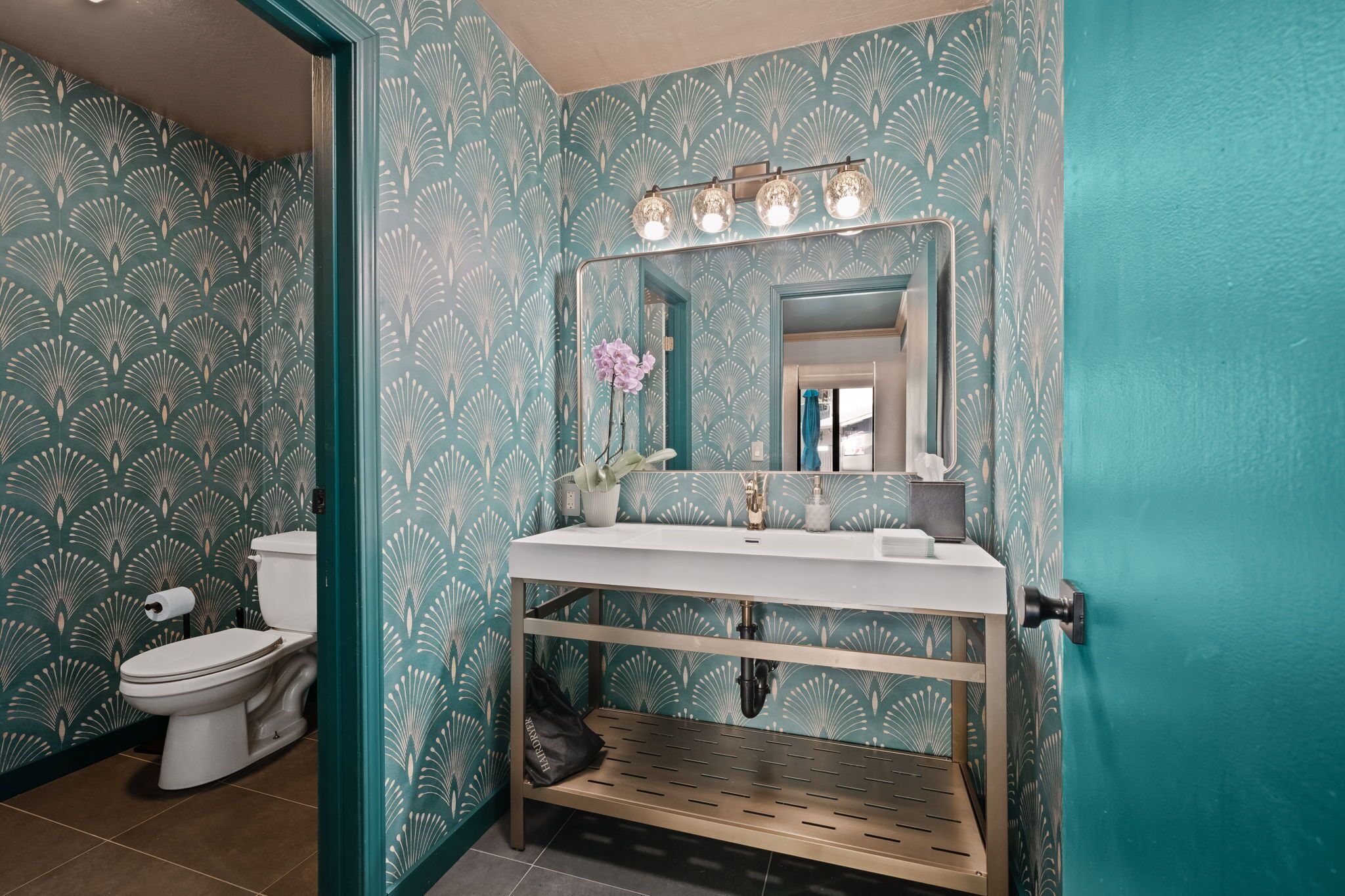 A bathroom with a white sink, a mirror with lights, a toilet, and patterned wallpaper.