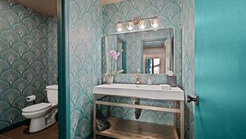 A bathroom with a white sink, a mirror with lights, a toilet, and patterned wallpaper.
