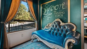 A room with a blue velvet sofa, a framed sign on the wall, and a window with curtains.