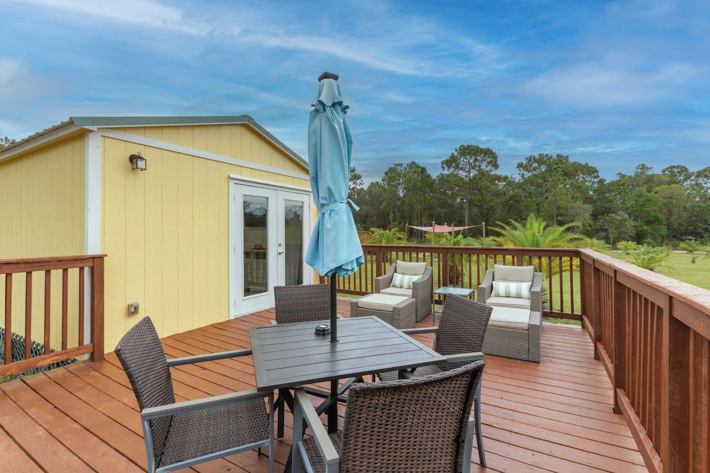A deck with a table and chairs, an umbrella, and a small building with a door.