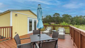 A deck with a table and chairs, an umbrella, and a small building with a door.
