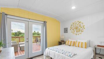 A bedroom with a bed, a desk, and a balcony with outdoor furniture.