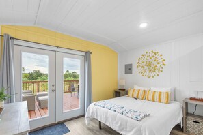 Un dormitorio con cama, escritorio y balcón con mobiliario exterior.
