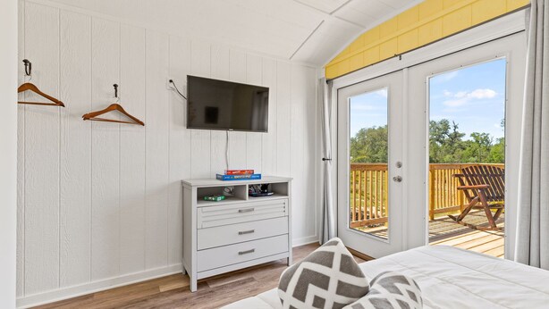 Une chambre à coucher comprenant un lit, une commode, un téléviseur et une porte-fenêtre coulissante donnant sur un balcon.