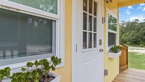 Un bâtiment jaune avec une porte et des fenêtres blanches, une terrasse en bois et un jardinier avec des plantes vertes.
