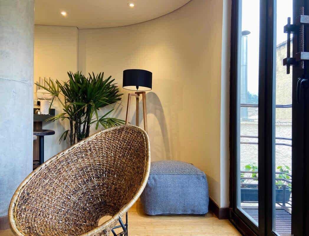 A room with a wicker chair, a small ottoman, a floor lamp, and a view of a balcony.