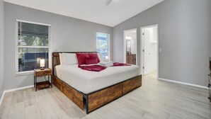 Un dormitorio con cama, mesita de noche, ventilador de techo y dos ventanas.