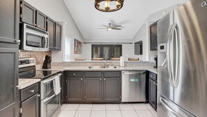 Una cocina moderna con armarios oscuros, electrodomésticos de acero inoxidable, encimera de granito y ventilador de techo.