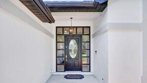 Una entrada de casa con una puerta principal oscura, un pequeño porche y un accesorio de luz decorativo sobre la puerta.