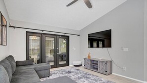 Una sala moderna con un sofá modular, un televisor de pantalla plana montado en la pared y un ventanal corredizo que da a un espacio exterior.