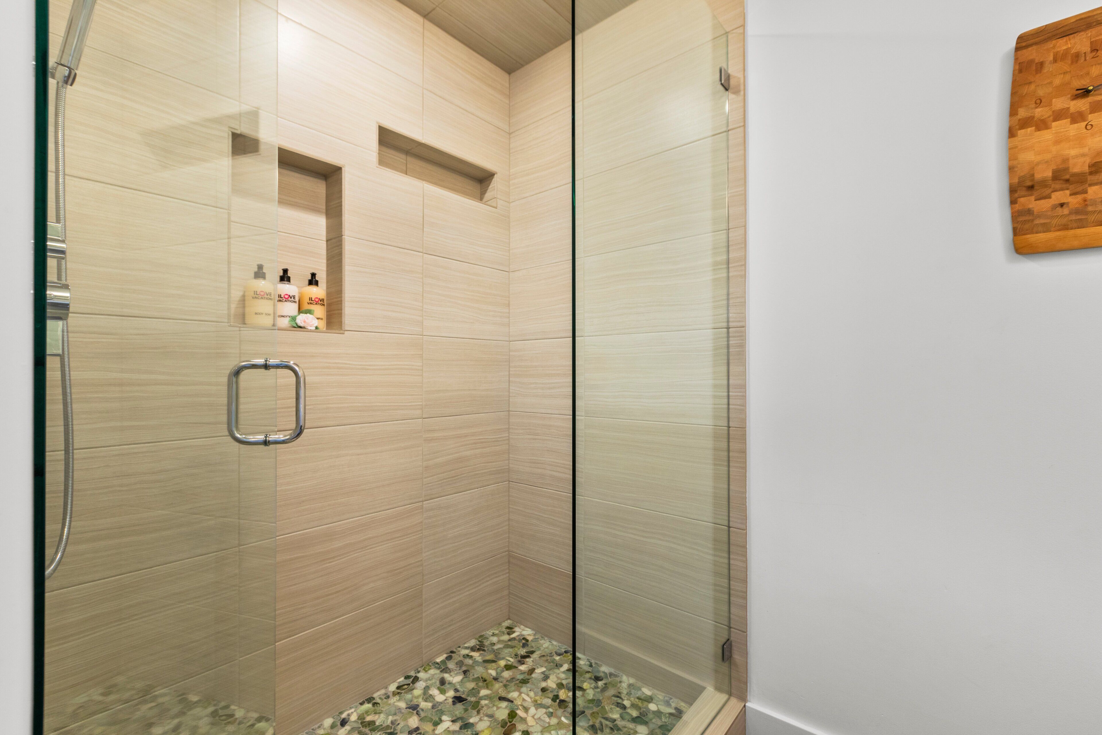 Una ducha moderna con puerta de cristal, cabezal metálico y un estante pequeño con artículos de aseo.