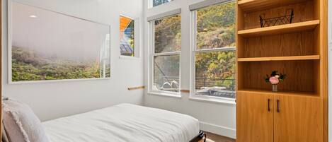A bedroom with a bed, a wooden bookshelf, and large windows.