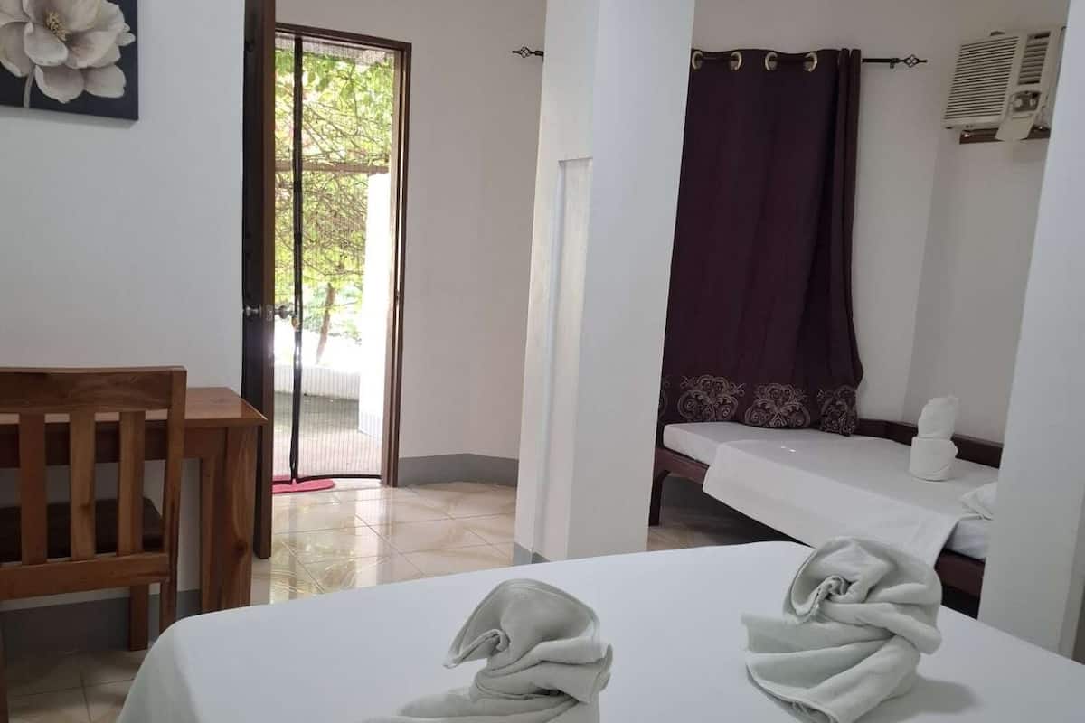 A hotel room with a bed, a wooden chair, a bathroom with a shower curtain, and a door leading to an outdoor area.