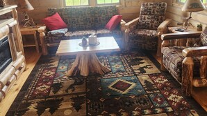 A cozy cabin interior with a wooden floor, a central coffee table, patterned sofas, and a fireplace. - Charming 2-bedroom cabin in Carey with AC, WiFi (Carey)