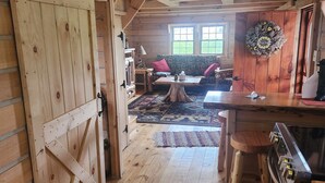 A wooden cabin interior with a dining area, kitchen, and a cozy seating space with a window. - Charming 2-bedroom cabin in Carey with AC, WiFi (Carey)