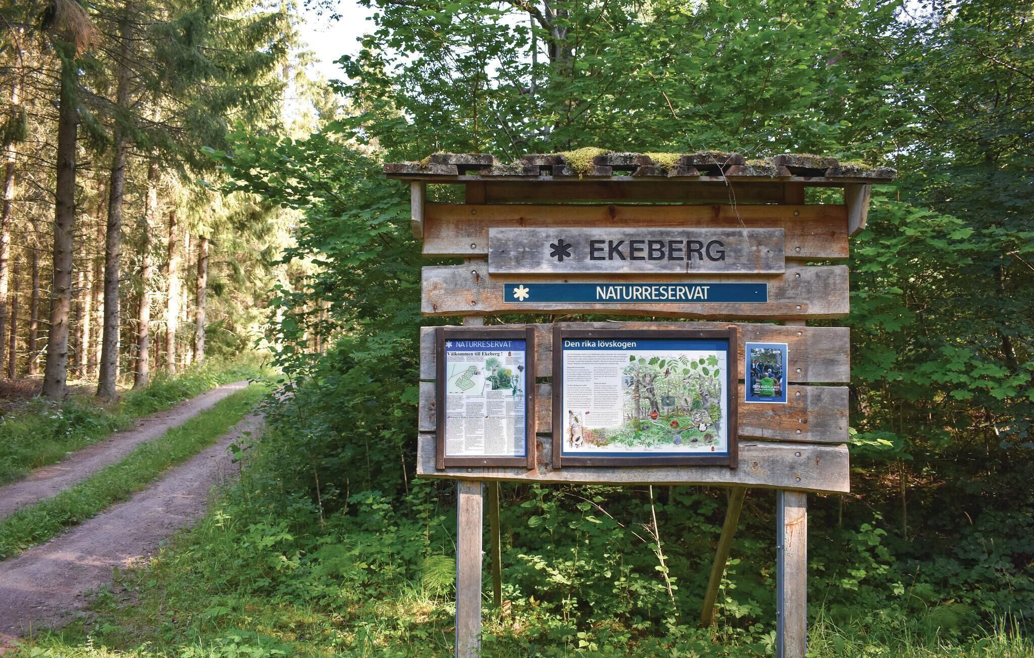 Un cartel de madera con 'EKEBERG NATURRESERVAT' y paneles informativos en un área boscosa.