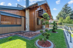 Una casa moderna con fachada de piedra, revestimiento de madera y un jardín cuidado con arbustos podados y un camino pavimentado.