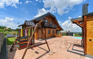 A wooden cabin with a sloped roof, a patio with a pool, and a colorful play structure.