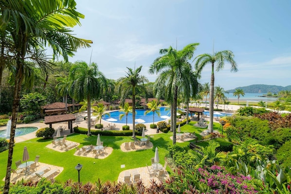 A resort with a central swimming pool, multiple lounge areas, and a view of the beach.