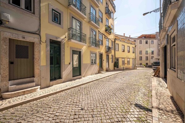 Una calle empedrada bordeada de edificios amarillos, cada uno con una puerta y ventanas verdes.