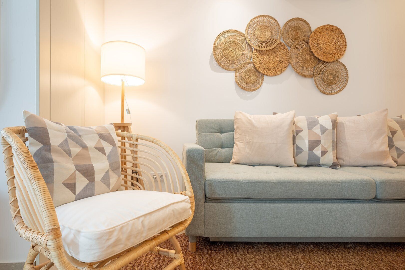 Ein Wohnzimmer mit einem Korbstuhl, einem grauen Sofa und einem an der Wand hängenden Webkunstwerk.