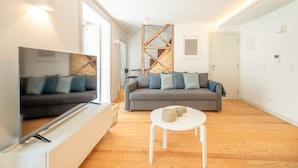 A modern living room with a grey sofa, a white coffee table, and a TV on a stand.