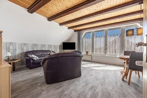 Una sala de estar moderna con techo de madera, un sofá de cuero, un televisor y un comedor con una mesa y sillas.