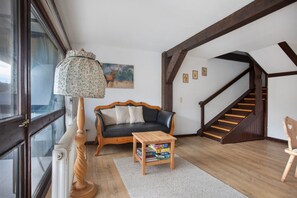 Una sala de estar con un sofá, una mesita con libros, una lámpara, una escalera y una ventana.