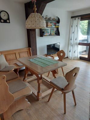 Una habitación acogedora con una mesa de madera, sillas, un sofá, un televisor y una estantería.