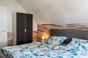 Ein Schlafzimmer mit einem Bett, einem Kleiderschrank, einem Nachttisch mit Lampe und einem Holz-Kopfteil.