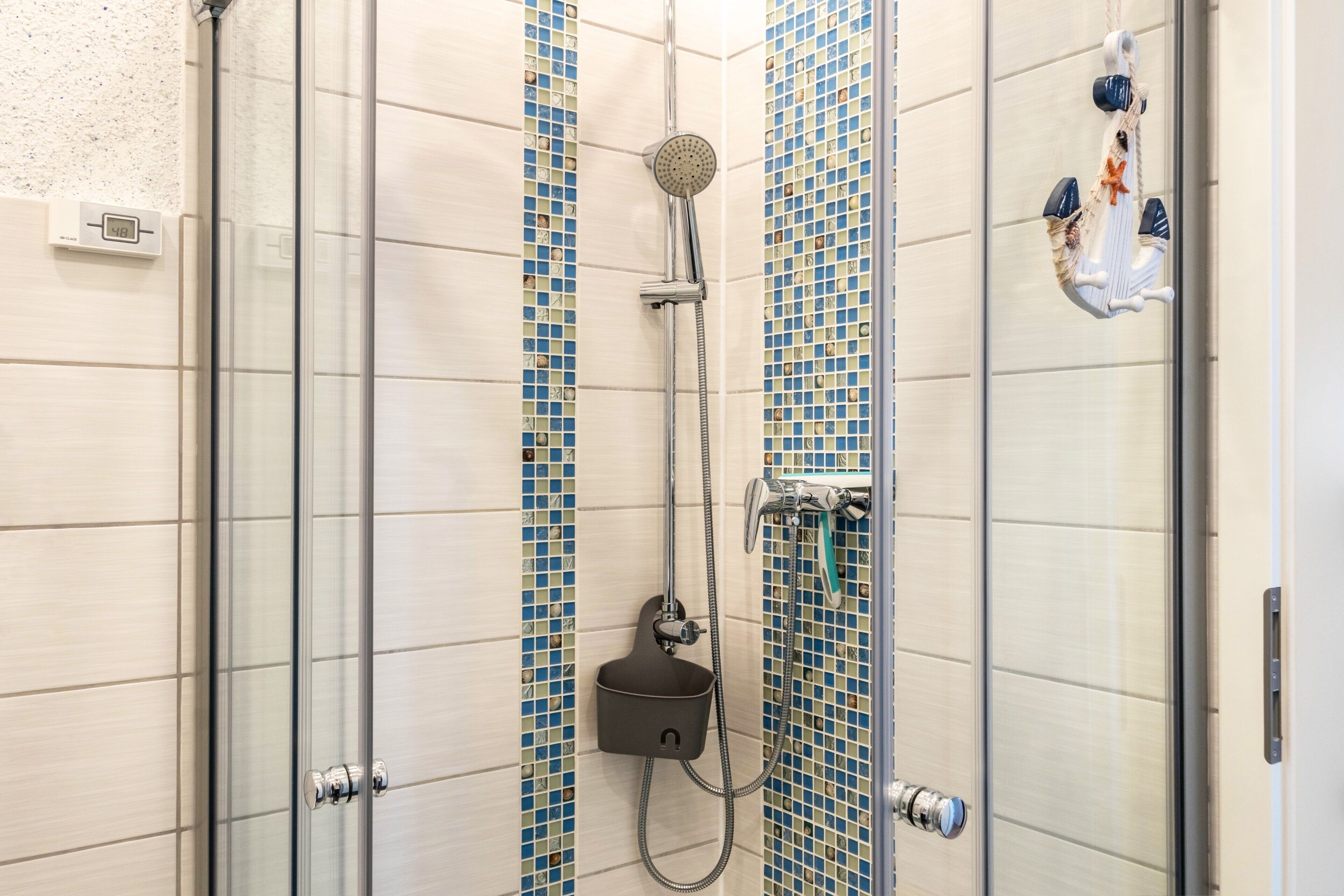 A shower with a handheld showerhead, a wall-mounted control panel, and a glass door.