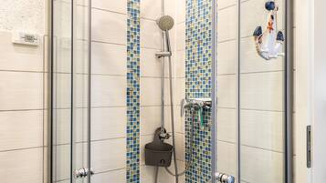 A shower with a handheld showerhead, a wall-mounted control panel, and a glass door.