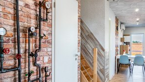 A modern interior with exposed brick walls, a wooden staircase, and a dining area with chairs. - Apartment 'Fewo Kaso' with Private Garden, Wi-Fi and Air Conditioning (Ihlow)